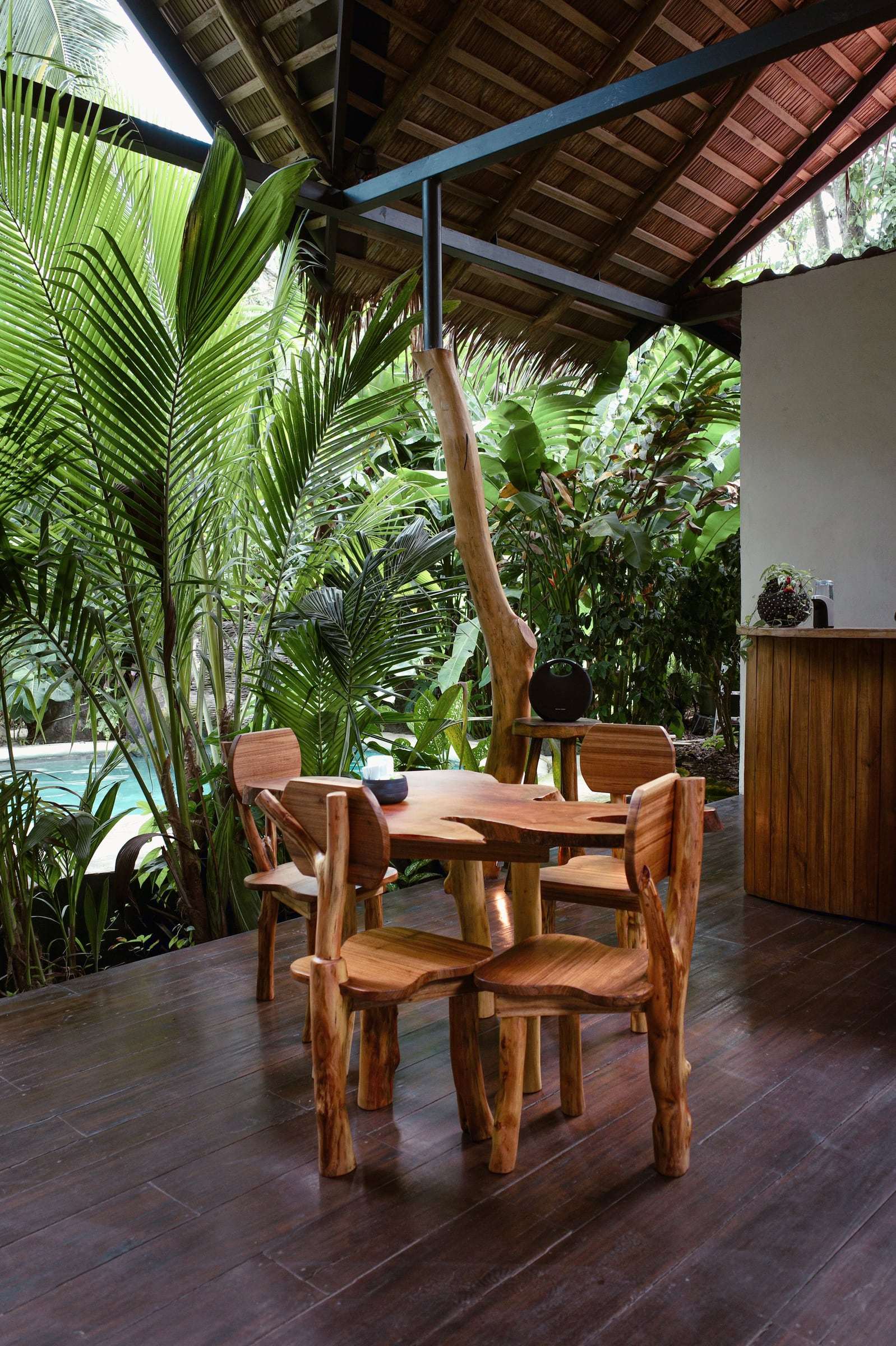 Hand-carved solid-wood table and chairs on the rancho's wooden deck, with the pool and palms behind