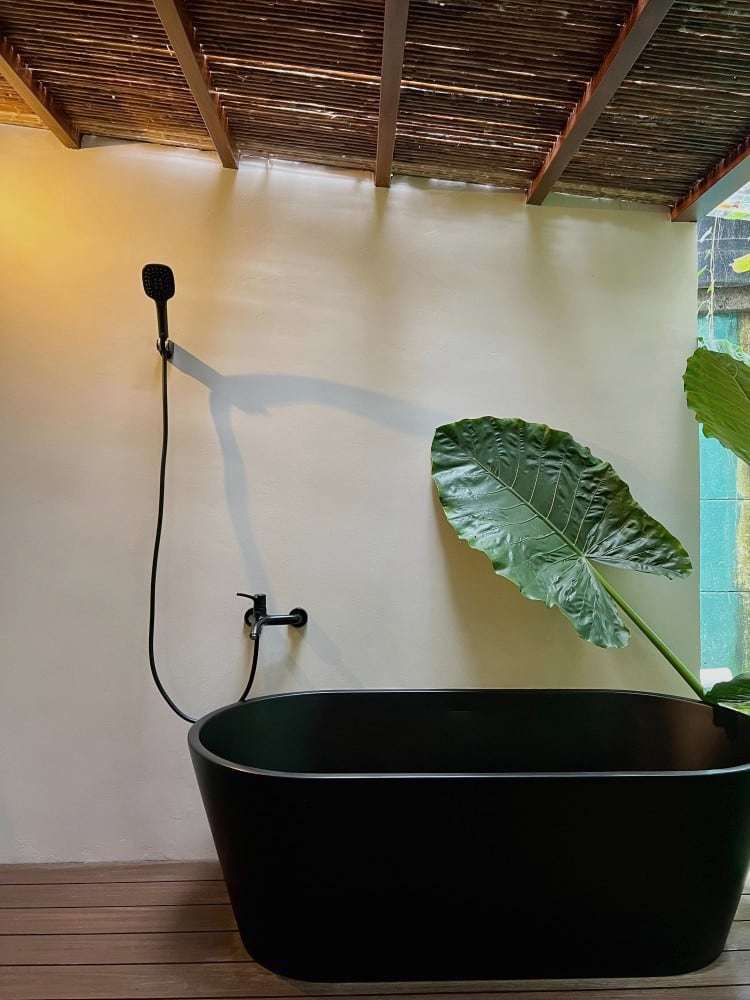 Grand Oasis Suite: black freestanding tub on the private deck beside a giant elephant-ear leaf
